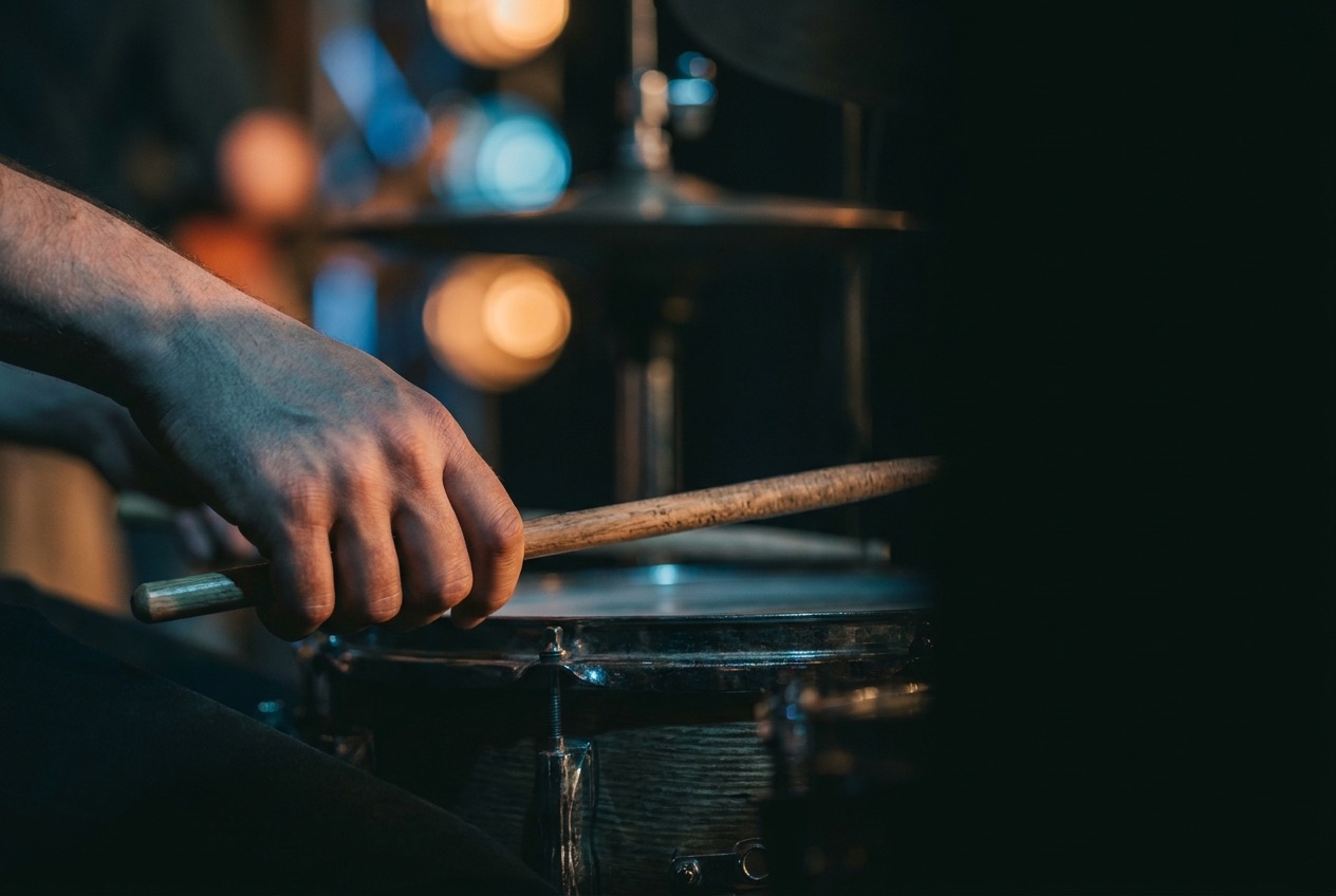 A hand striking a snare drum with a drumstick, lit in cool blue stage light